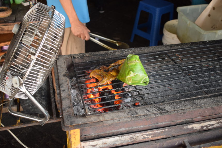 grilling bebek bakar and nasi bakar over flaming charcoal being blown by electric fan