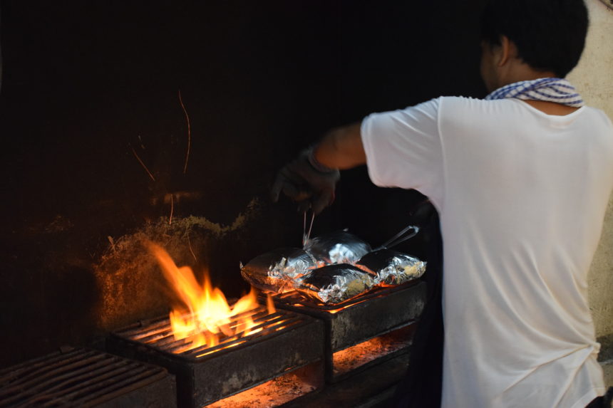 Man grilling seafood parcels over roaring charcoal flame