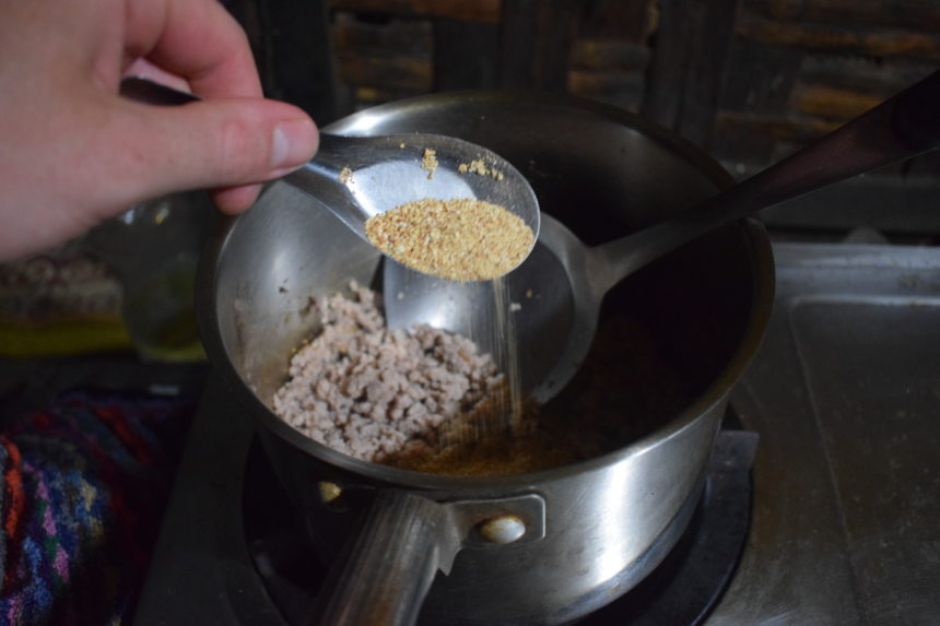 toasted sticky rice (khao neow) being poured onto meat in frying pan whilst cooking pork larb