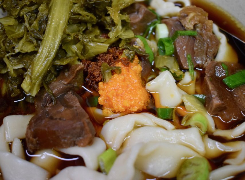 Spoonful of bright orange chilli butter melting gently into beef broth of bowl of best beef noodle in Ximending