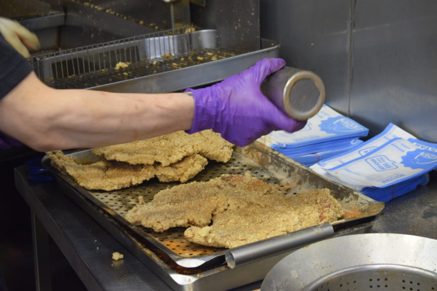 Man shaking seasoning over fried chicken after taking out of fryer