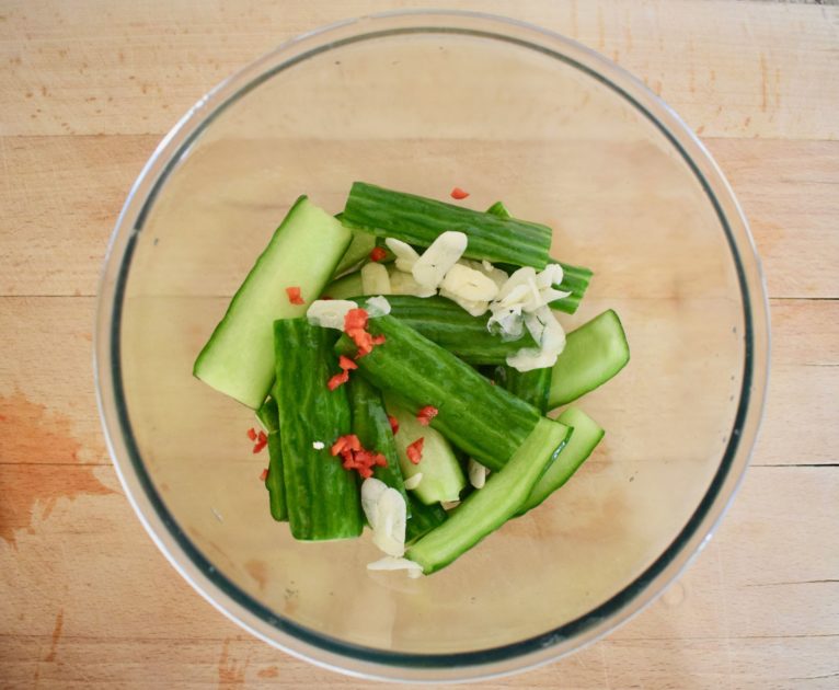 Cucumber batons in bowl coated in chopped garlic, chilli and vinegar ready for second stage of marination