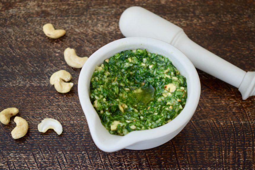 Homemade Thai basil pesto with cashews in a mortar surrounded by scattered cashews and a pestle