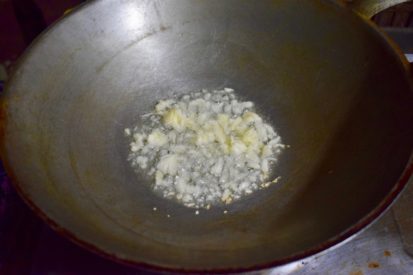 5 cloves of crushed garlic frying in oil in wok for pad fak tong