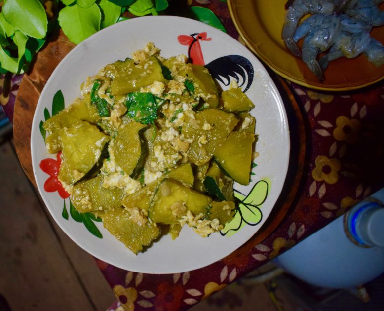 Finished thai pumpkin stir fry (pad fak tong) on table with kaffir lime leaves and prawns