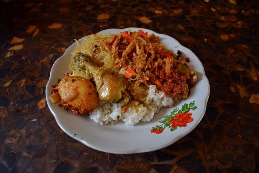 A plate of nasi campur from Bali with roast chicken, vegetables and a red blob of sambal terasi goreng on the side