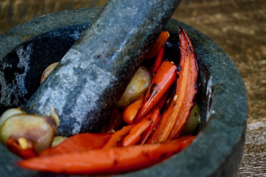 Grinding charred chillies and shallots in a pestle and mortar to make Indonesian sambal terasi
