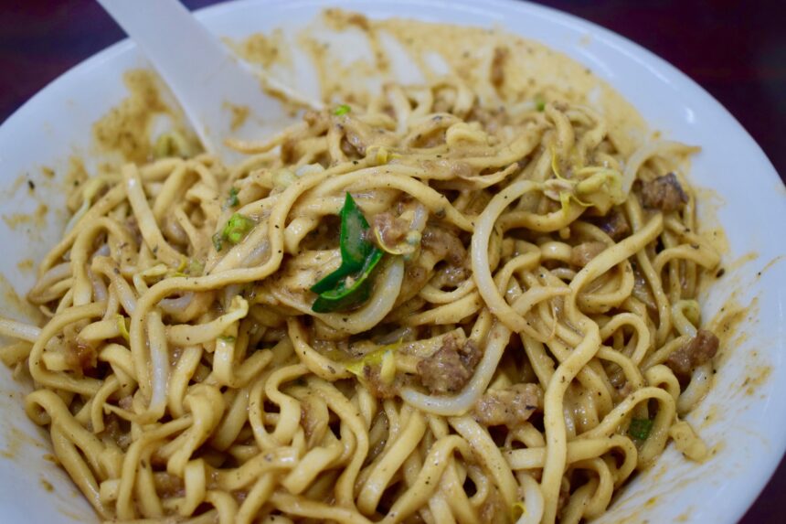 Close-up of noodles, beansprouts and spring onions coated in thick Chinese sesame sauce