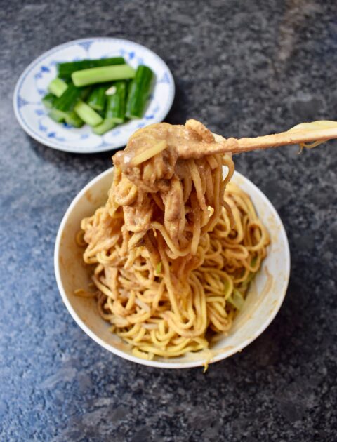 The result of my Taiwanese cold noodles recipe with noodles coated in glossy sesame sauce being pulled by chopsticks