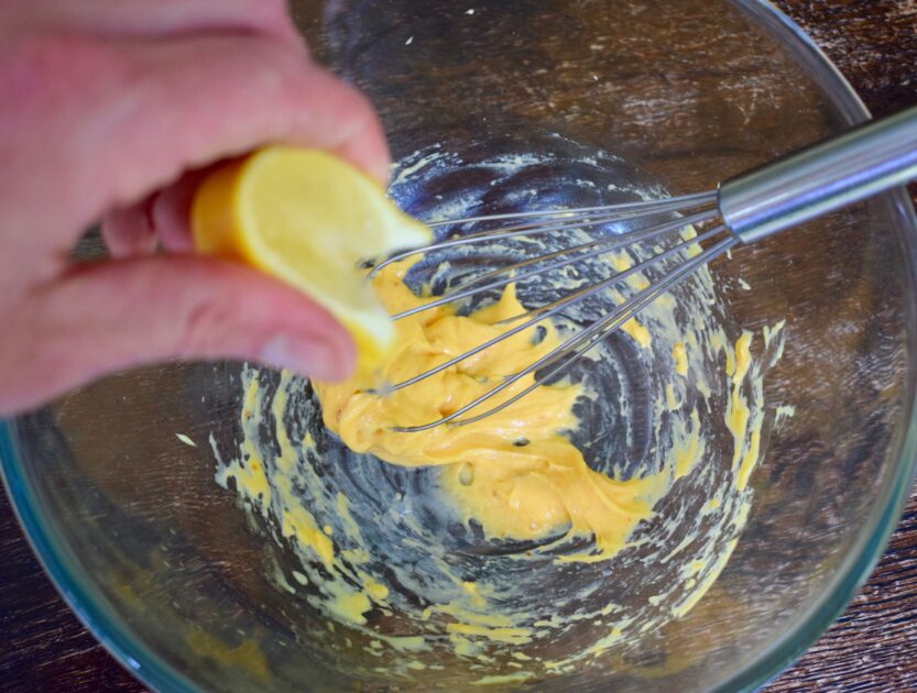 Squeezing a lemon segment into a half-made bowl of nduja mayo to loosen the mayonnaise