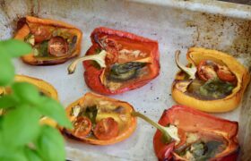 Italian roasted peppers with anchovies in a metal baking tray with basil in foreground