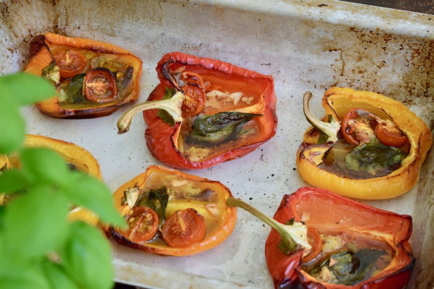 Italian roasted peppers with anchovies in a metal baking tray with basil in foreground