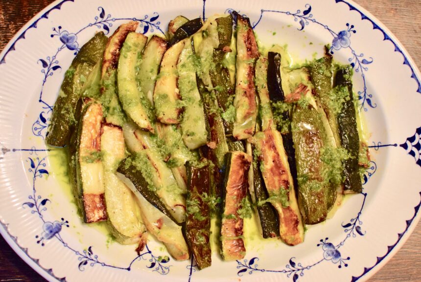 Easy roasted zucchini on a blue plate covered in olive oil, lemon and basil