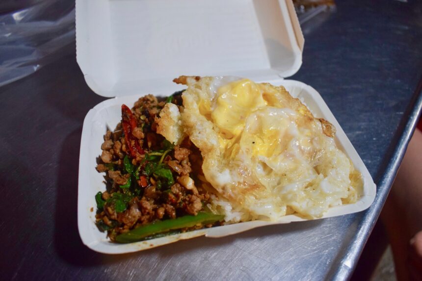 A styrofoam container filled with a pad kra pao moo along with prik nam pla and a fried egg, eaten in Chiang Mai, Thailand