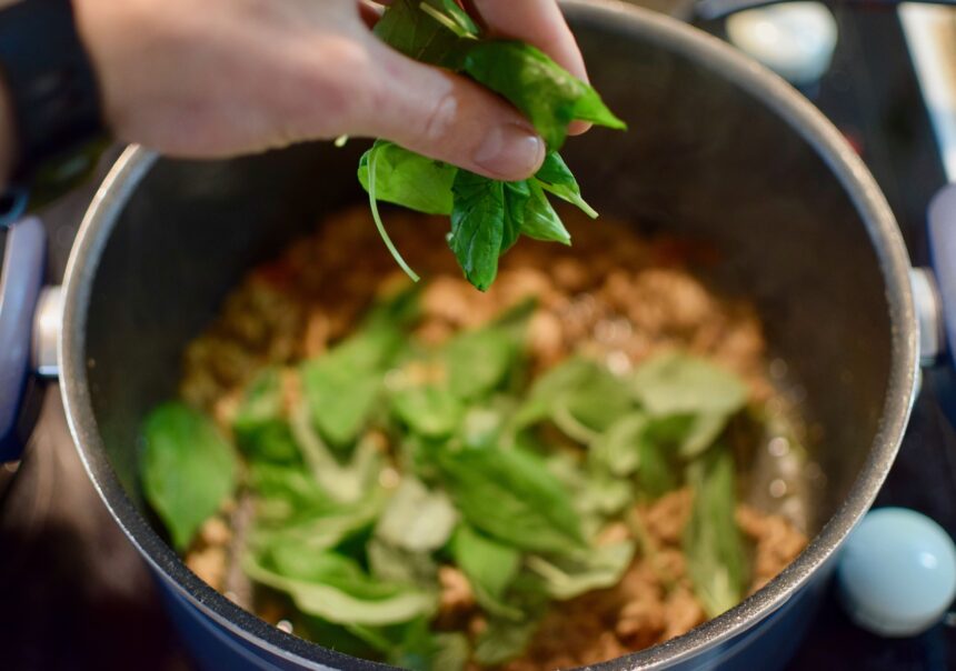 Dropping holy basil leaves into the pad kra pao moo saap at the final stage of cooking