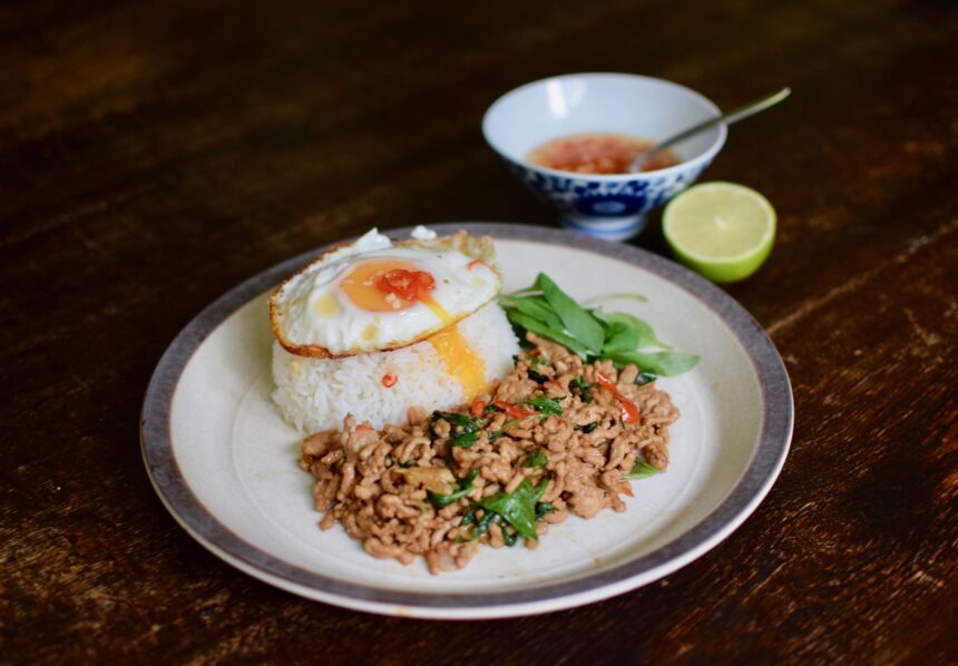 Thai basil minced pork (pad kra pao moo saap) with white rice and a fried egg on a table with lime and a small bowl of prik nam pla