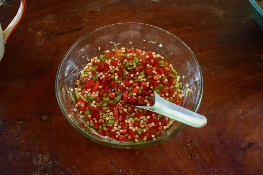 A small glass bowl prik nam pla (Thai chilli dipping sauce) on a wooden table in Thailand